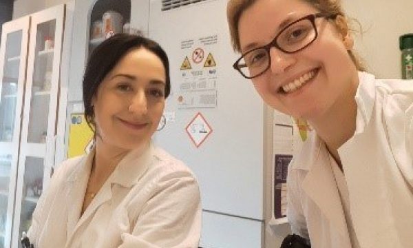 2 researchers in the lab, with white lab coats, smiling