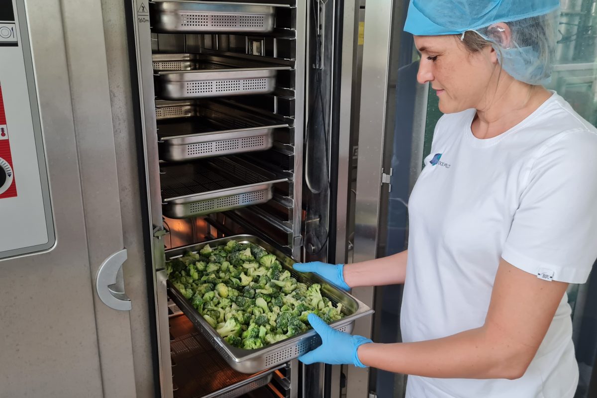 Een medewerker van Food Pilot haalt een school broccoli uit een industriële steamer
