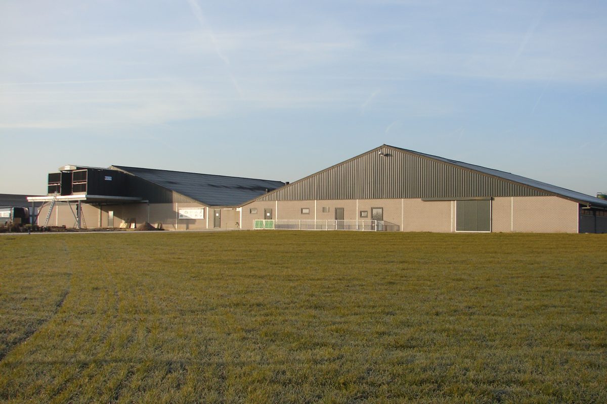 Varkensstal met luchtwasser met op de voorgrond een akker met gras.