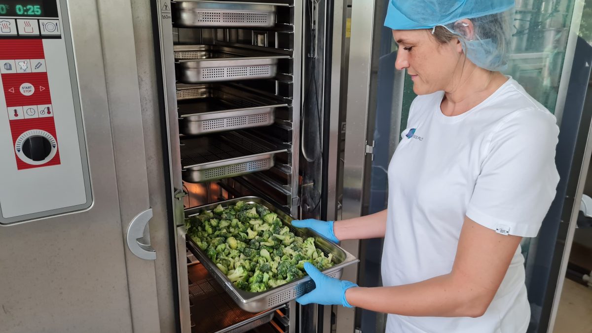 Een medewerker van Food Pilot haalt een school broccoli uit een industriële steamer