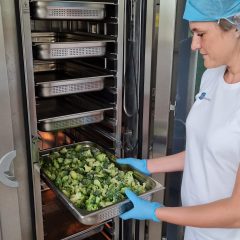 Een medewerker van Food Pilot haalt een school broccoli uit een industriële steamer