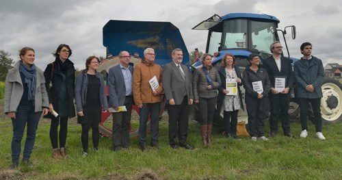 Groepsfoto met Vlaams minister van Omgeving, Natuur en Landbouw Joke Schauvliege op een grasakker met in de achtergrond een blauwe tractor