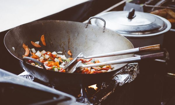 Een wokpan op een vuur, er liggen groenten in te bakken