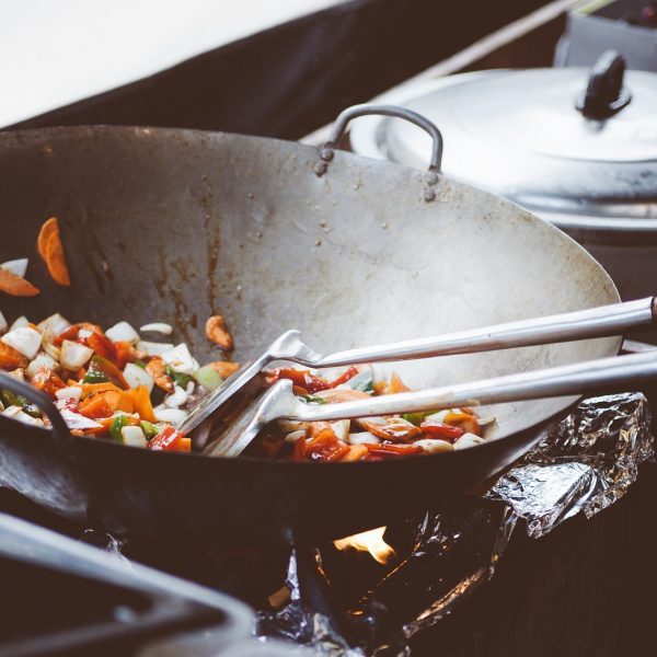 Een wokpan op een vuur, er liggen groenten in te bakken