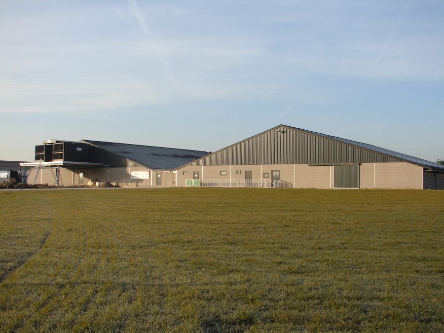 Varkensstal met luchtwasser met op de voorgrond een akker met gras.